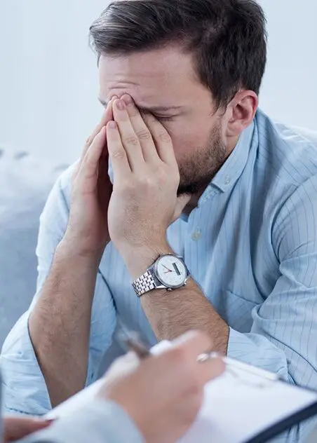 A man sitting on the couch with his hands over his face.