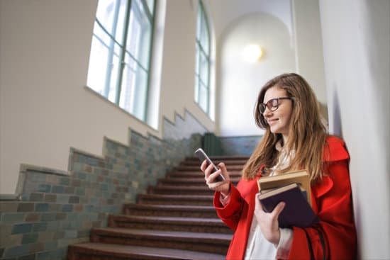 A woman in red jacket holding book and cell phone.