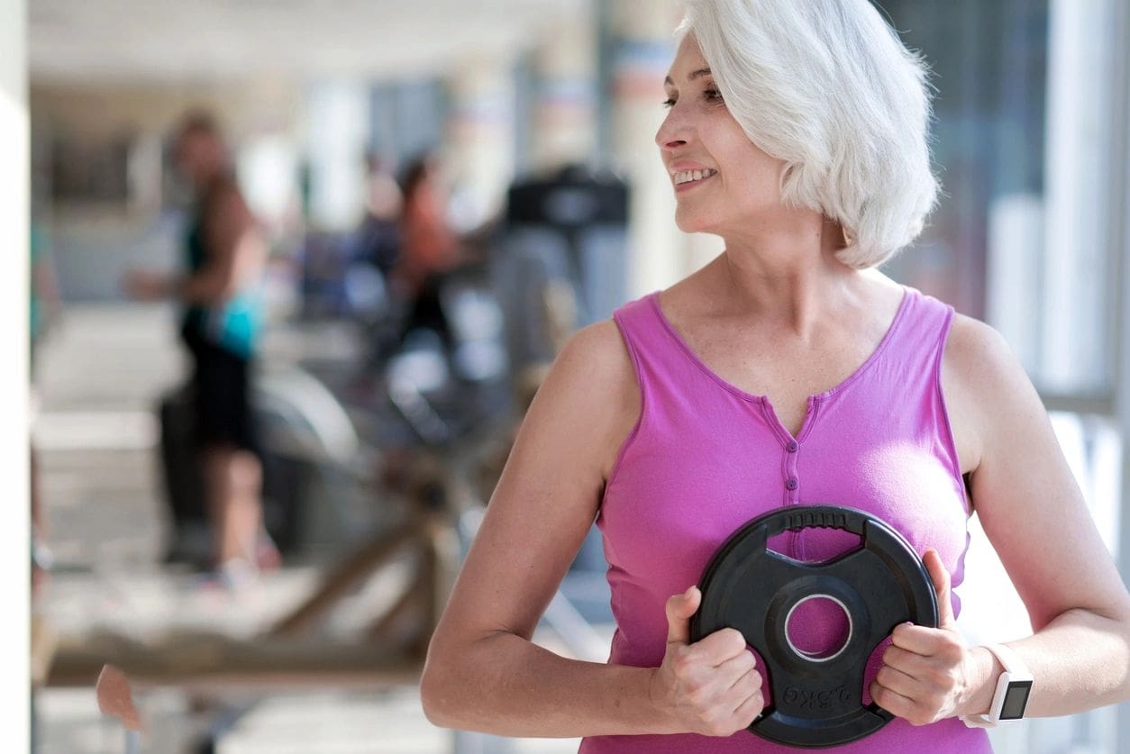 Happy fitness. Beautiful active woman turning head and smiling while exercising with plate in a gym.